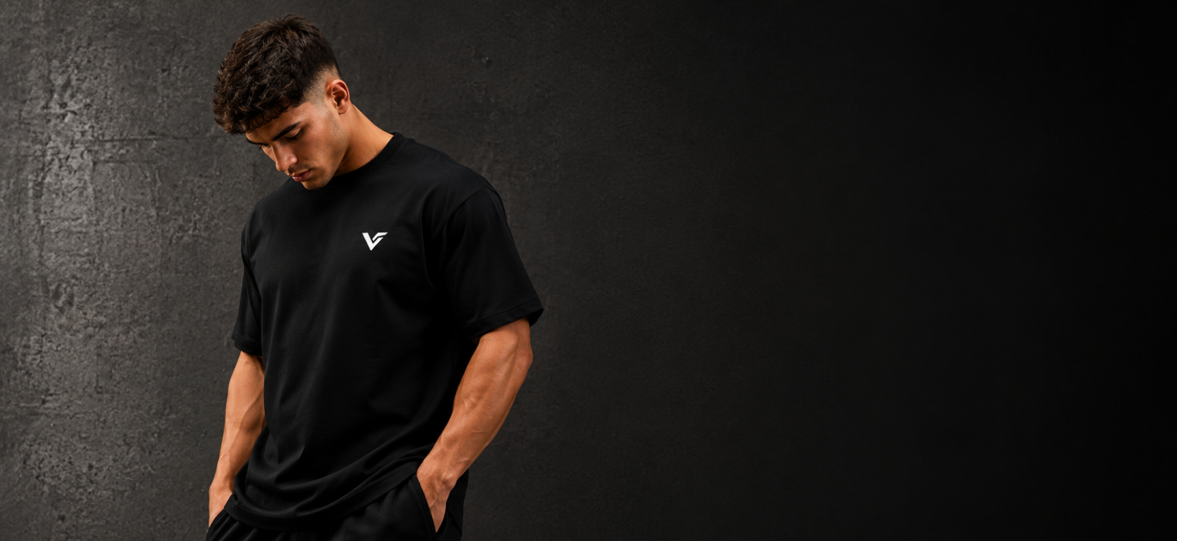 A man wearing a black athletic t-shirt and matching shorts with a small white logo, posing against a dark textured studio background.
